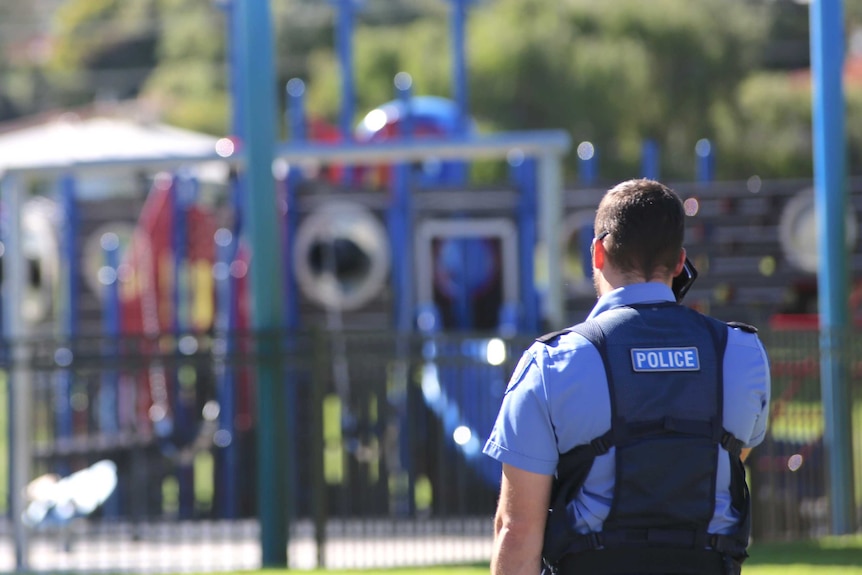 The back of a police officer standing in a children's park.