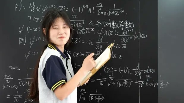 A girl standing in front of a black board. 