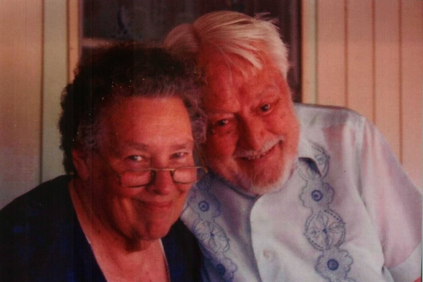 Old woman with glasses and old man with white hair and beard smile at the camera in close up photo.