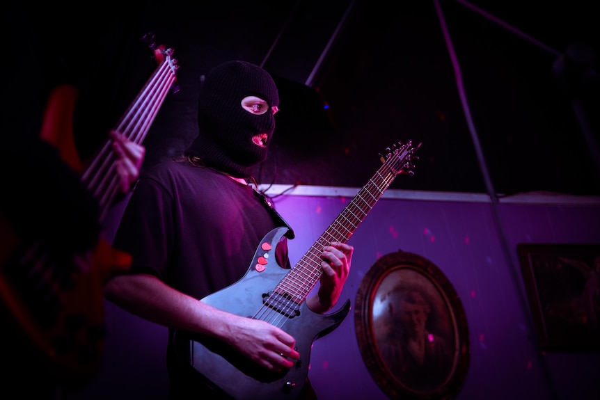 Band member wearing a mask and playing the guitar. 