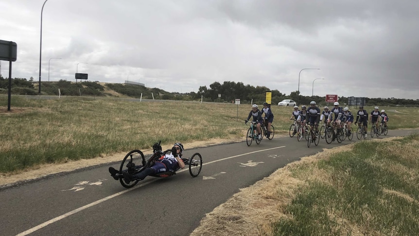 Charles Brice on his modified pedal-powered device with support riders on a walking path.