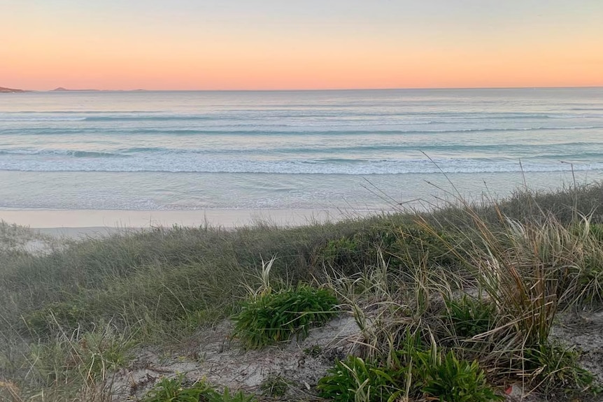 Sunset at Fourth Beach, with an orange sky, dunes and waves pictured