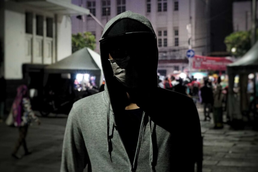 "Bintang" poses for a photo in a dark street with a mask on making his face unidentifiable.