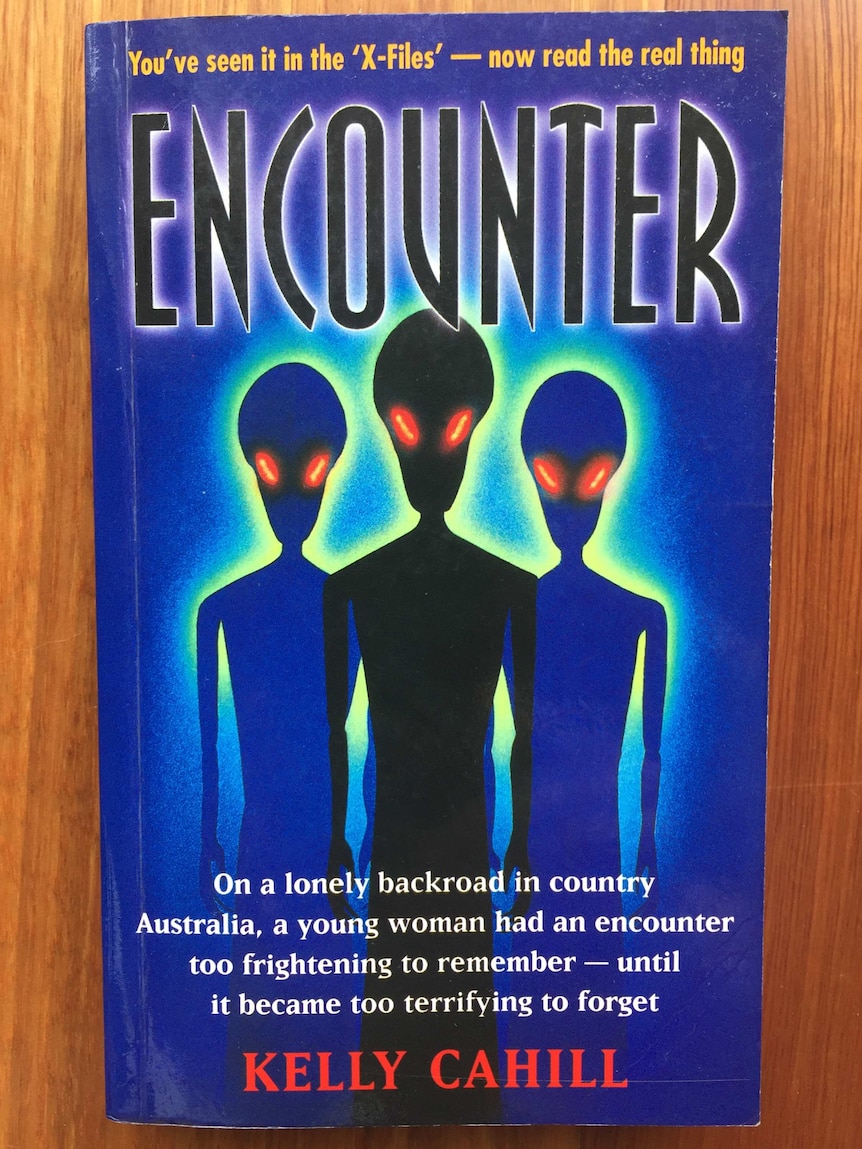 Glowing eyed aliens appear on the front cover of a paperback novel.