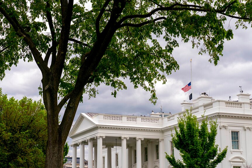 You look up at the White House on a cloudy day, with the US flag flying above it at half mast.