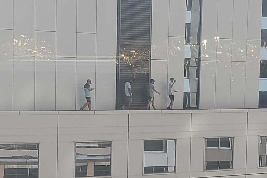Four boys walk on ledge of a high-rise