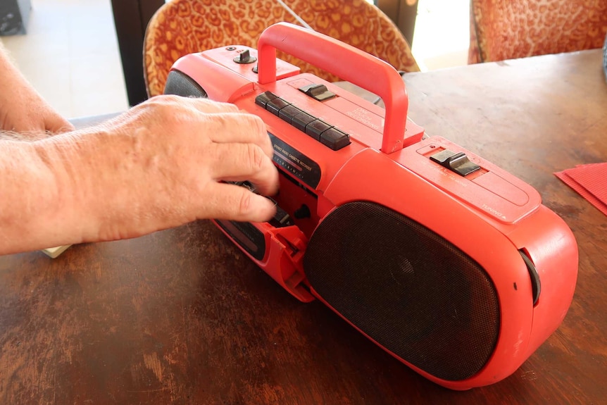 A man places a tape in a red cassette player