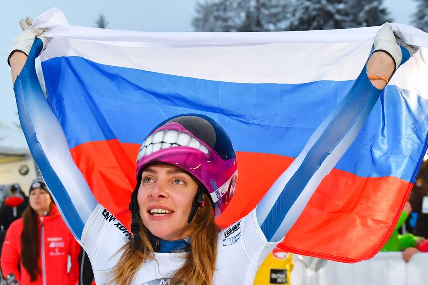 Elena Nikitina holds up a Russian flag and looks in to the distance.
