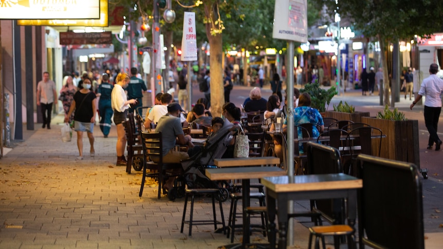 People eat in alfresco dining on a street in a busy entertainment precinct