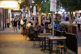 People eat in alfresco dining on a street in a busy entertainment precinct