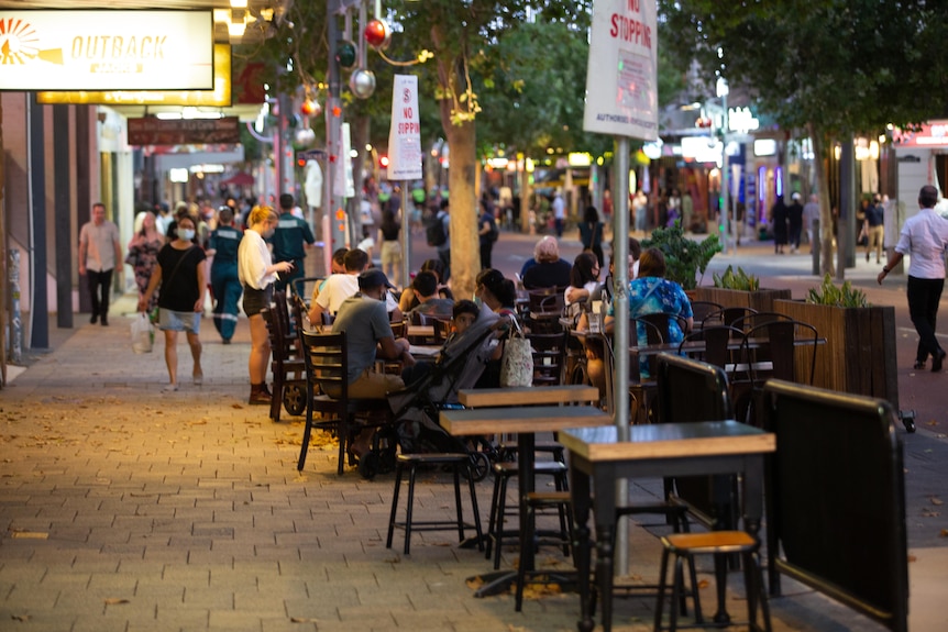 People eat in alfresco dining on a street in a busy entertainment precinct