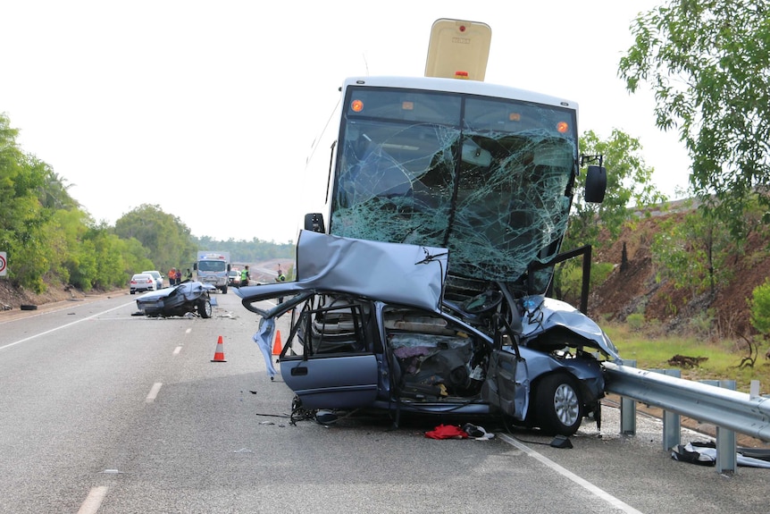 The front half of a car is pictured wedged under a bus, with the back half seen in the distance, at a crash site in Darwin.