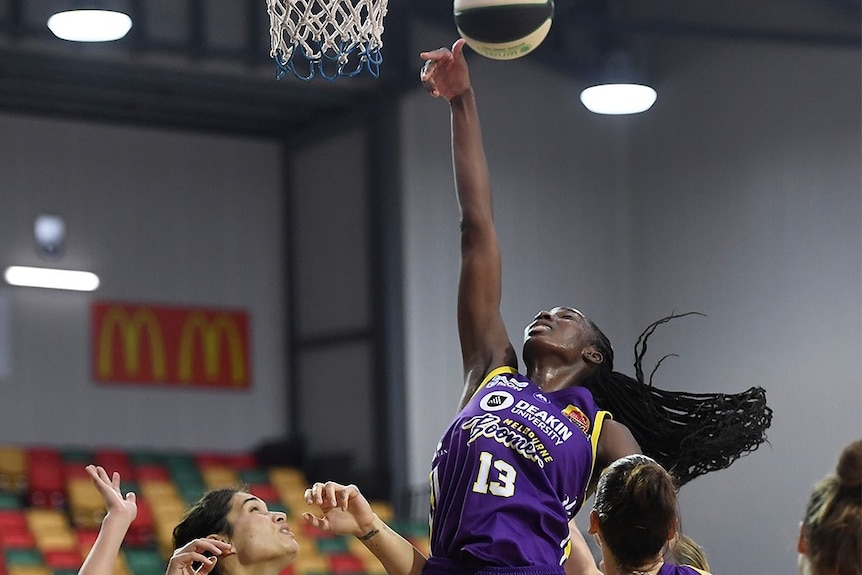 A woman leaps above three others and shoots for a basket.