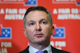 Chris Bowen wearing a suit and tie in front of a Labor party promotional backdrop.