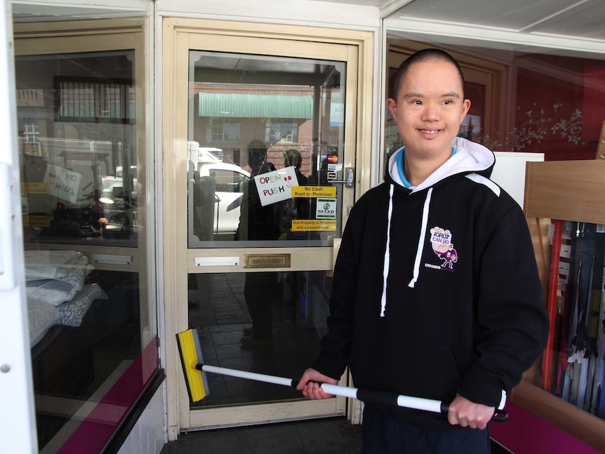 Jordyn Trelfo stands in front of a shop window with a window cleaner in his hands.