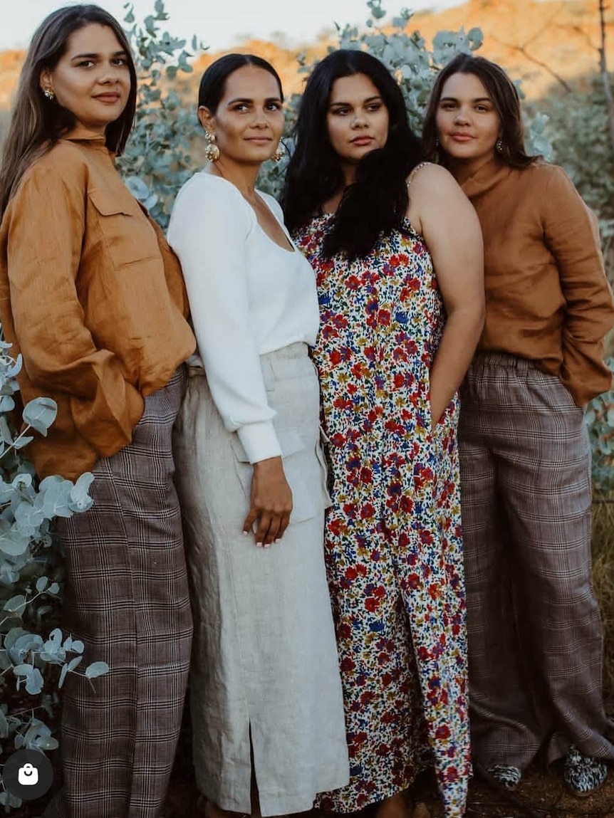 Indigenous women wearing neutral colored clothes pose for photo