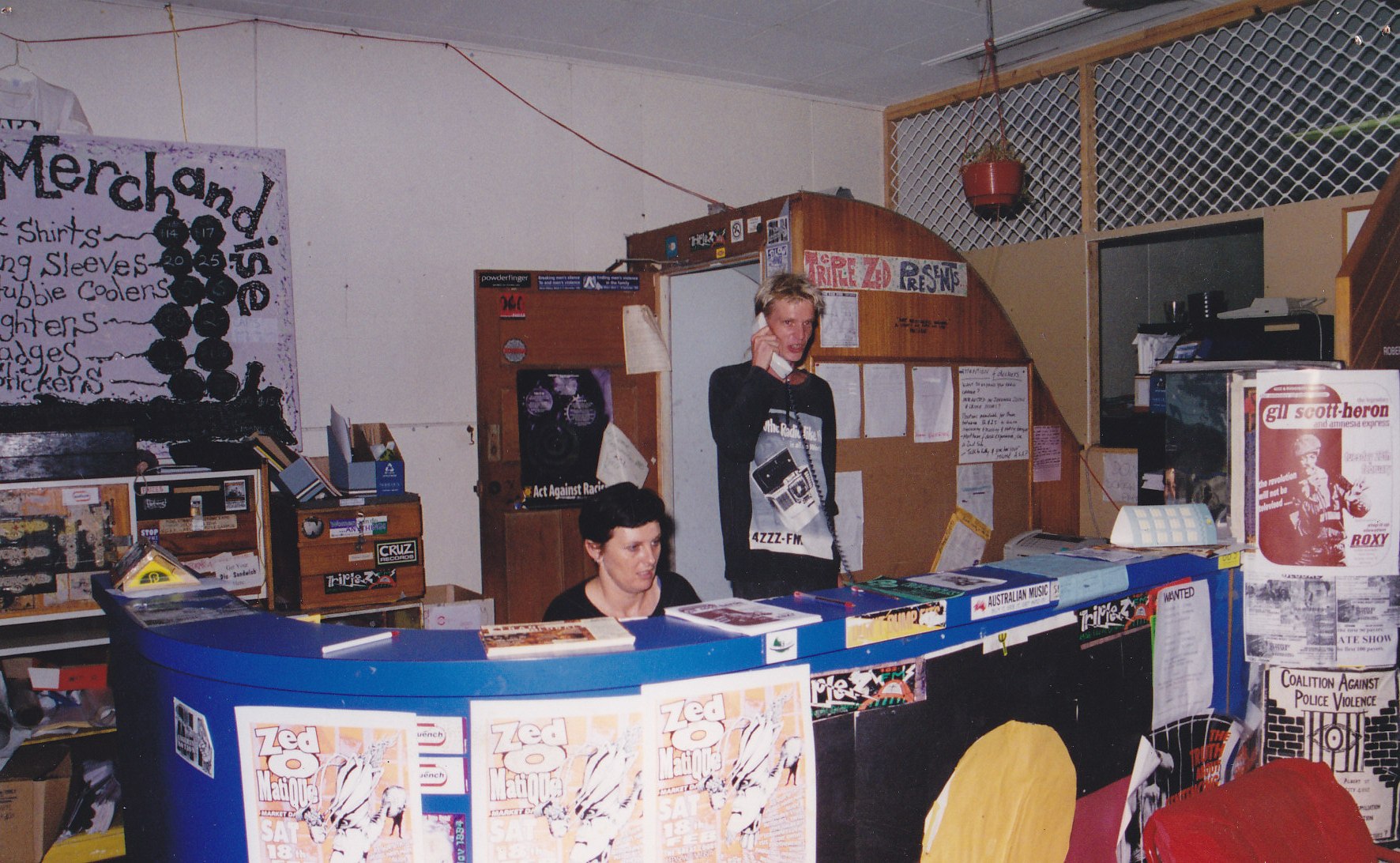 Photo of young man answering phone at desk manned by young woman in a makeshift office space