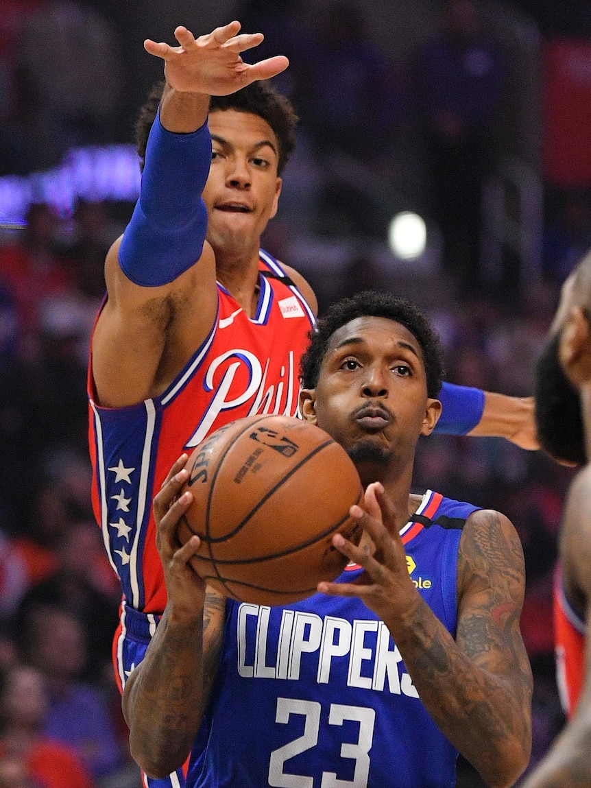 Philadelphia 76ers player Matisse Thybulle sticks his arm and hand out over the Cippers' Lou Williams, who has the basketball.