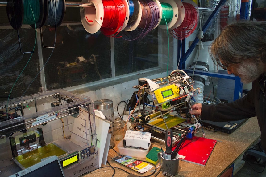 A man looks at one of two 3D printers