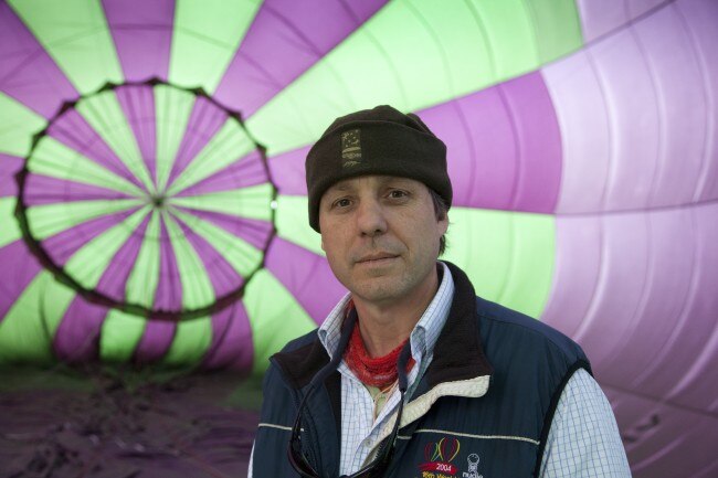 A man wearing a beanie stands in front of a partially inflated hot air balloon