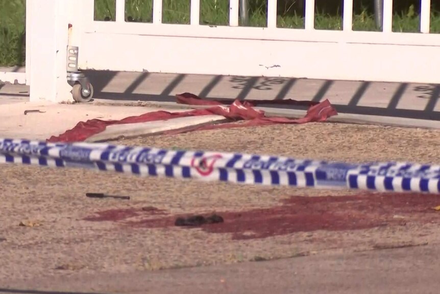A pool of blood on a footpath outside a suburban house. Police crime scene tape cordones off the area.
