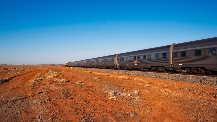 A train on a railway with red dirt in the foreground