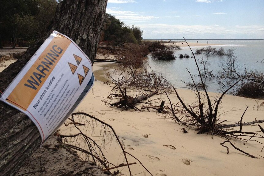 Warning sign on tree on beach at site of a near-shore landslide at Inskip Point on Queensland's Cooloola Coast