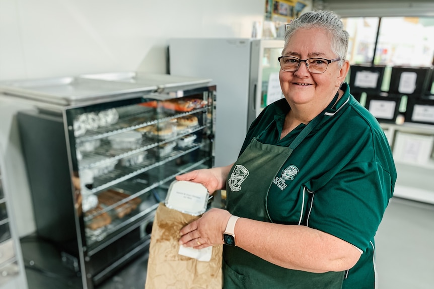 A woman in a tuckshop kitchen puts a meal into a brown bag