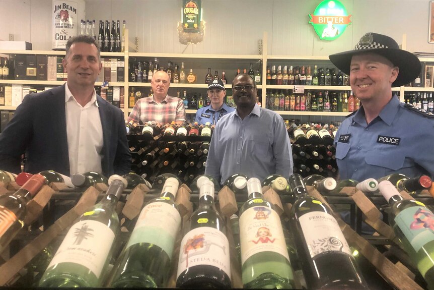 five people including two police officers in a liquor store, looking at camera, bottles infront
