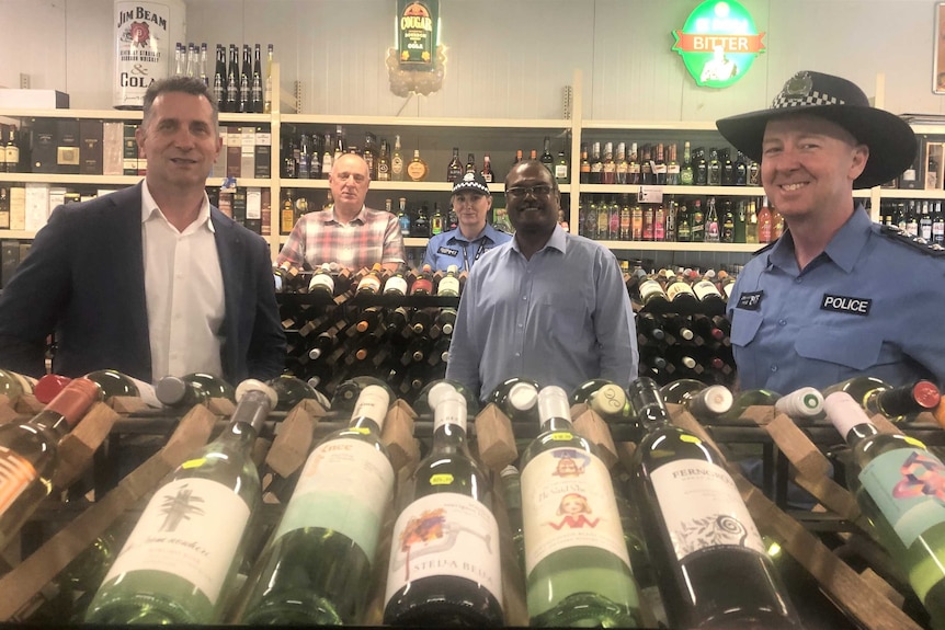 five people including two police officers in a liquor store, looking at camera, bottles in front.