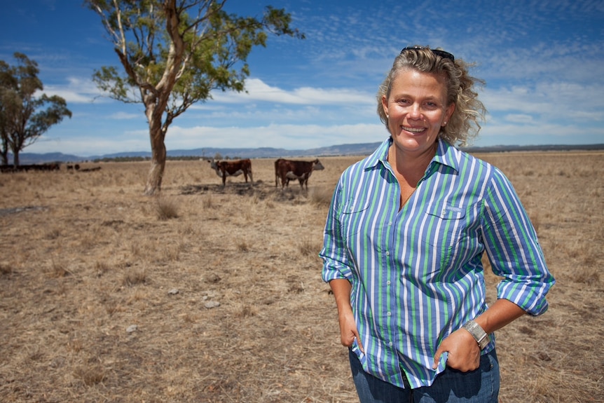 Woman with blonde hair stands in a paddock.