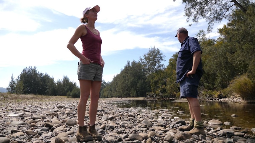 Lisa and Craig standing on dry river bed by small stream looking around hopelessly.