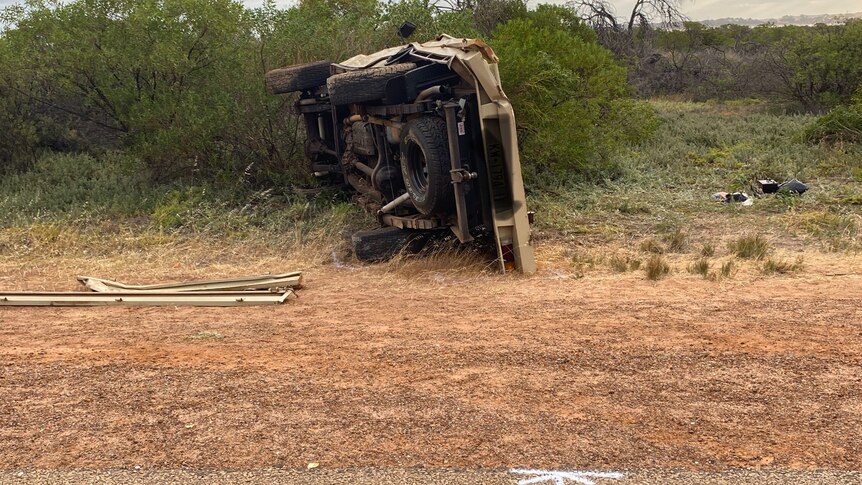 Four wheel drive vehicle on its side, next to a bitumen road and gravel