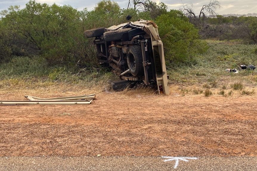Four wheel drive vehicle on its side, next to a bitumen road and gravel