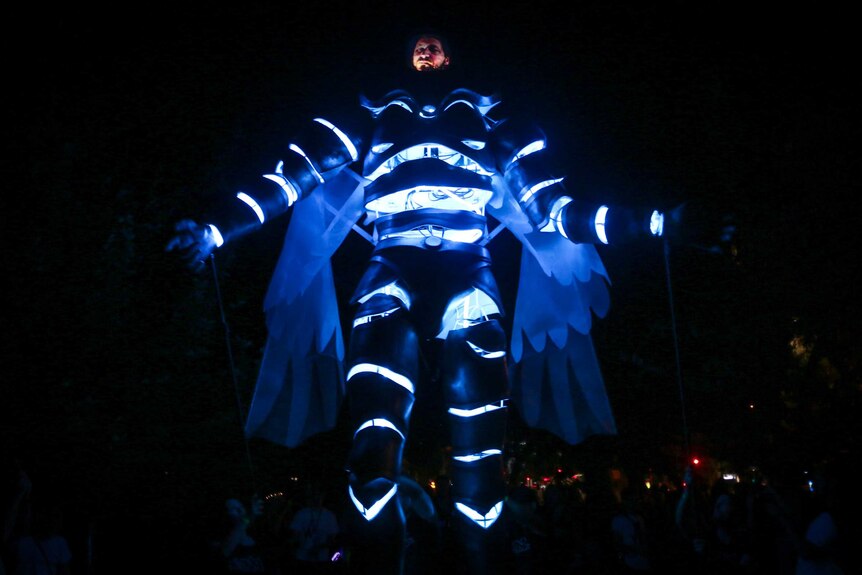 A man in a large space suit with glowing blue lights walks down the street in Melbourne.