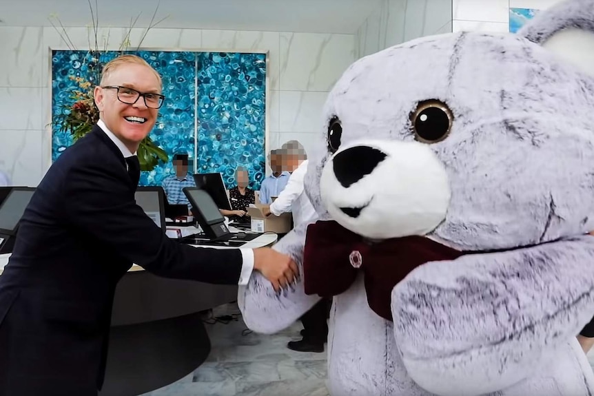 Man in suit grinning shakes hand of large costume bear in hotel foyer