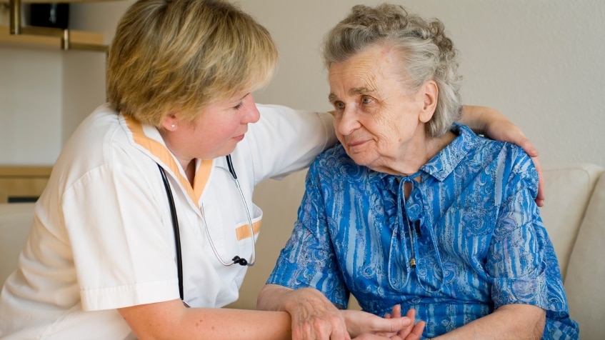 Nurse sitting with arm around elderly woman