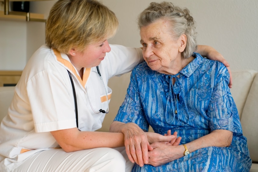 Nurse sitting with arm around elderly woman