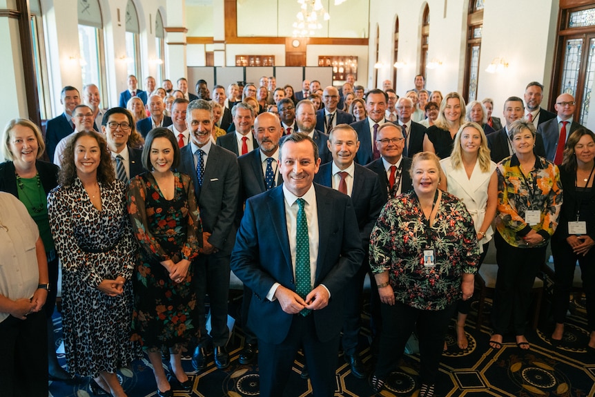 A large group of people standing up and smiling at the camera inside a room.