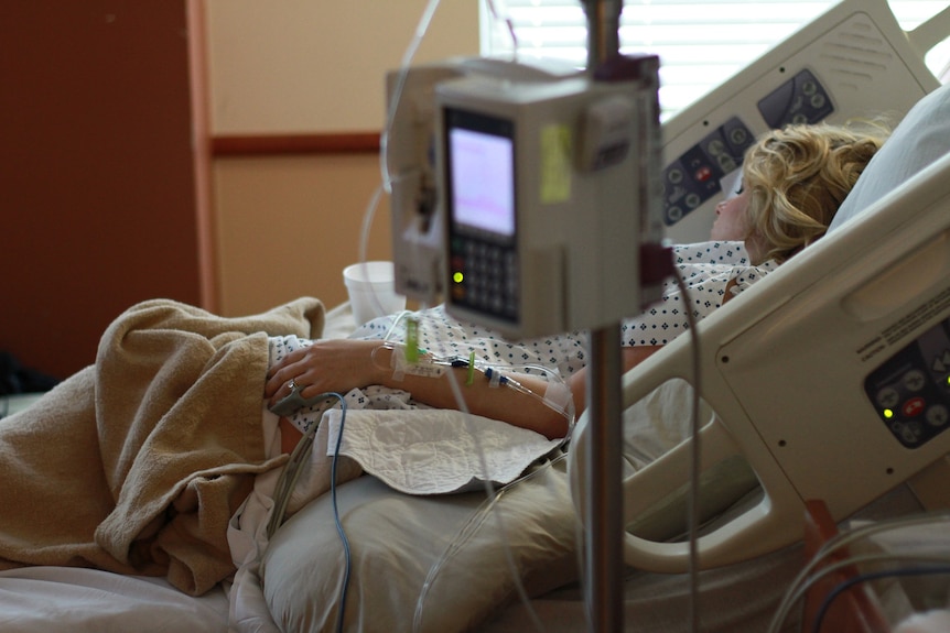 A woman lies in a hospital bed with a monitor in the foreground 