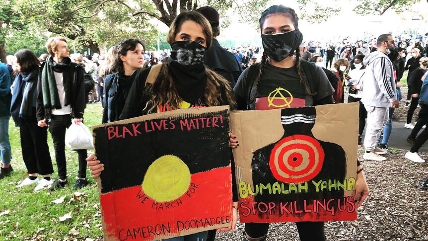 Two women, wearing face masks, hold signs at a Black Lives Matter protest