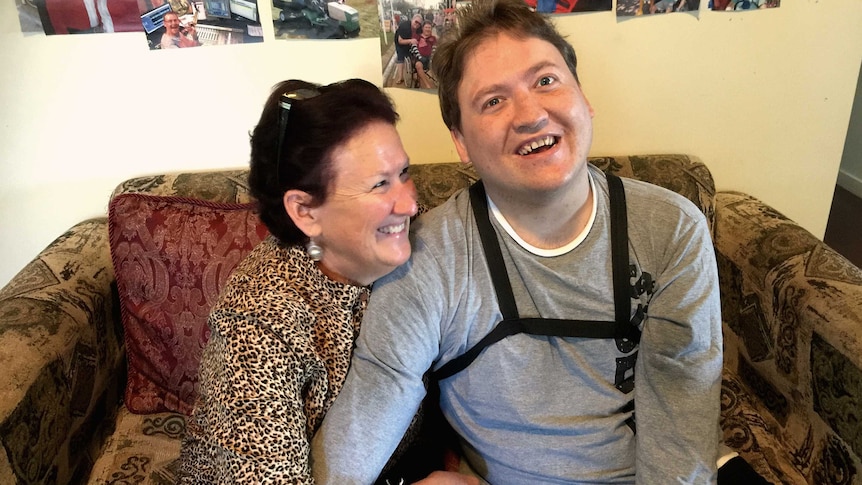 Mother looks lovingly at adult son, sitting together on the couch.