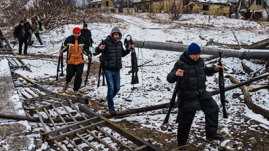 Ukrainian men in casual winter clothes carrying multiple rifles walk along broken bridge in the snow