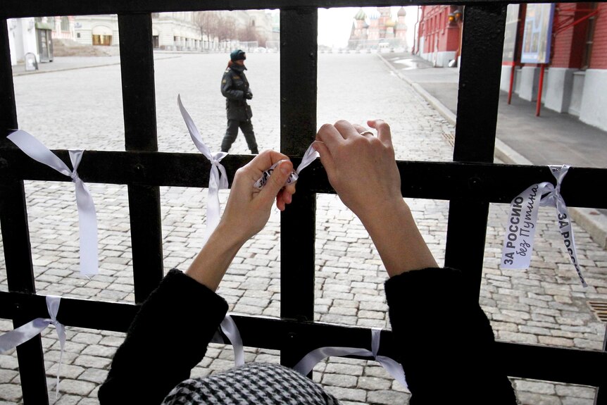 A woman ties a white ribbon to Red Square's Resurrection Gate.