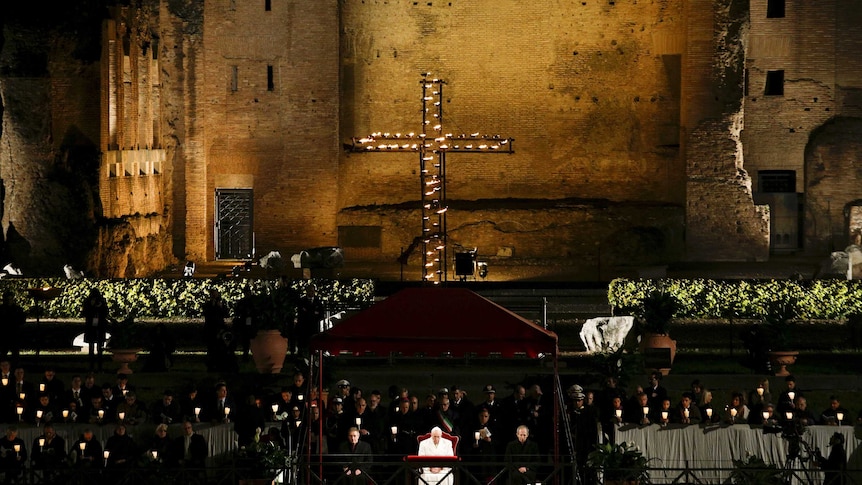 A cross  lights up in front of the Colosseum in Rome with large crowds in front