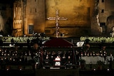 A cross  lights up in front of the Colosseum in Rome with large crowds in front
