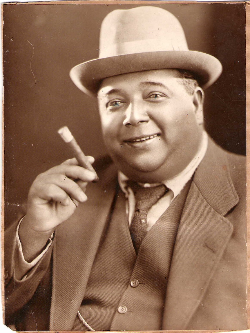 Smiling Indian man wearing a porkpie hat and holding a cigar in the early 1900s
