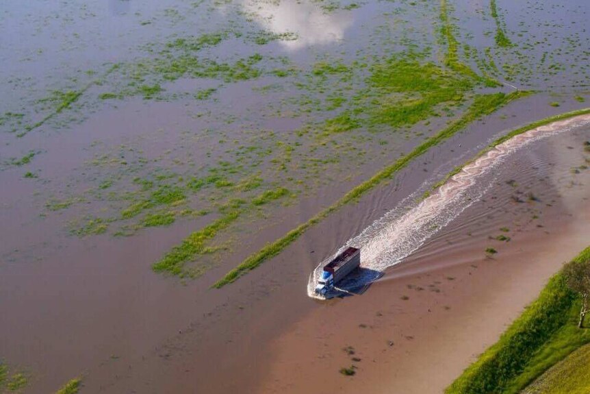 An aerial shot of flooded paddocks with a truck going through