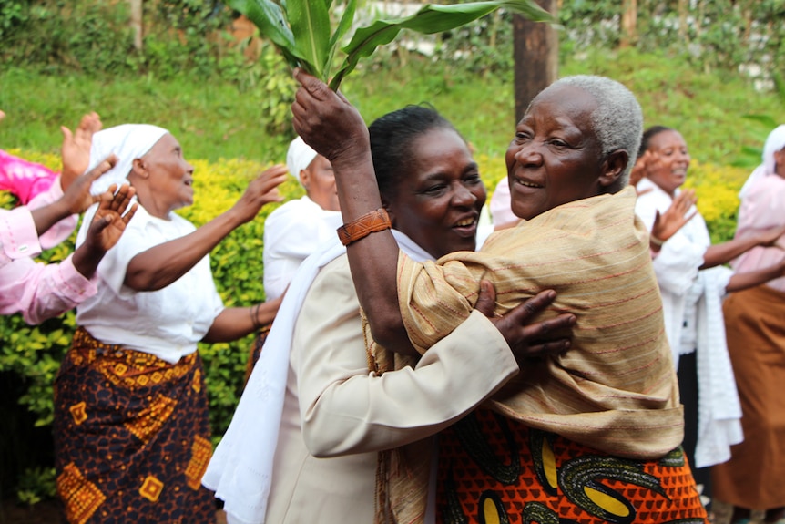 Two women hug with women dancing behind them