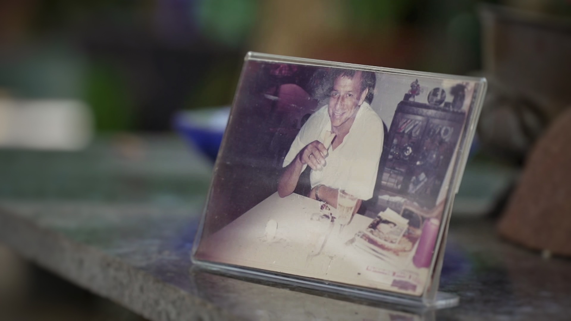 A photo frame on a marble kitchen counter that depicts a man leaning on a kitchen counter with a sandwich in hand.